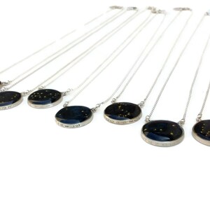 May include: A set of silver necklaces with round pendants featuring constellations and zodiac signs. The pendants are black with gold glitter and have the name of the constellation inscribed around the edge.