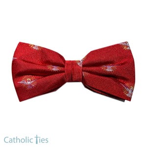 May include: A red bow tie with a repeating pattern of a dove with a golden halo. The bow tie is made of a textured fabric and has a classic butterfly shape. The text "Catholic Ties" is at the bottom.