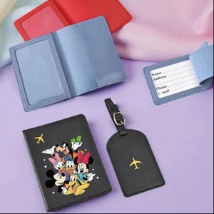 May include: A selection of travel accessories, including passport holders and luggage tags. The passport holders are in red and blue, and the black passport holder features a cartoon graphic. The black luggage tag has a gold airplane icon.