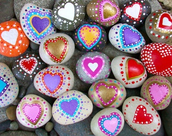 May include: A collection of painted heart-shaped rocks in various colors, including red, pink, purple, blue, yellow, and white. The rocks are decorated with dots and swirls.