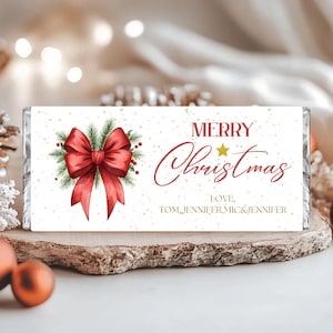 May include: A white candy bar wrapper with a red bow and Christmas message. The wrapper features a watercolor illustration of a red bow with green pine needles and the words "MERRY Christmas" in red script. The names "TOM, JENNIFER, MIC & JENNIFER" are also printed.