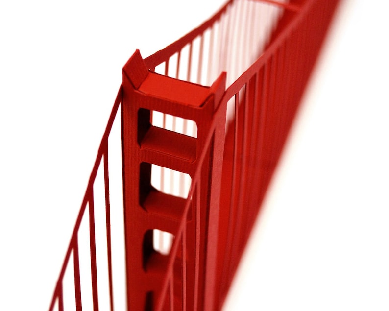 Closeup of the upper part of the Golden Gate bridge model features suspension cables and one of the towers. The 3d scale model is made out of red die-cut cardstock parts.