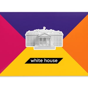 Product packaging for the White House paper model kit. The bright coloured cardstock envelope features four large triangles in yellow, magenta, purple and orange with an image of a finished model at the centre and the product title below.