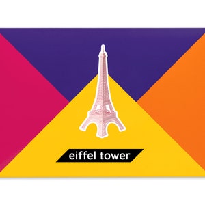 Product packaging for the Eiffel Tower paper model kit. A recangular bright coloured cardstock envelope features four large triangles in yellow, magenta, purple and orange with an image of a finished model at the centre and the product title below.