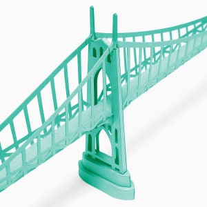 May include: A teal paper model of a suspension bridge. The bridge has a curved deck and two towers with arches.