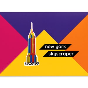 Product packaging for the New York Skyscraper paper model kit. The bright coloured cardstock envelope features four large triangles in yellow, magenta, purple and orange with an image of a finished model at the centre and the product title below.
