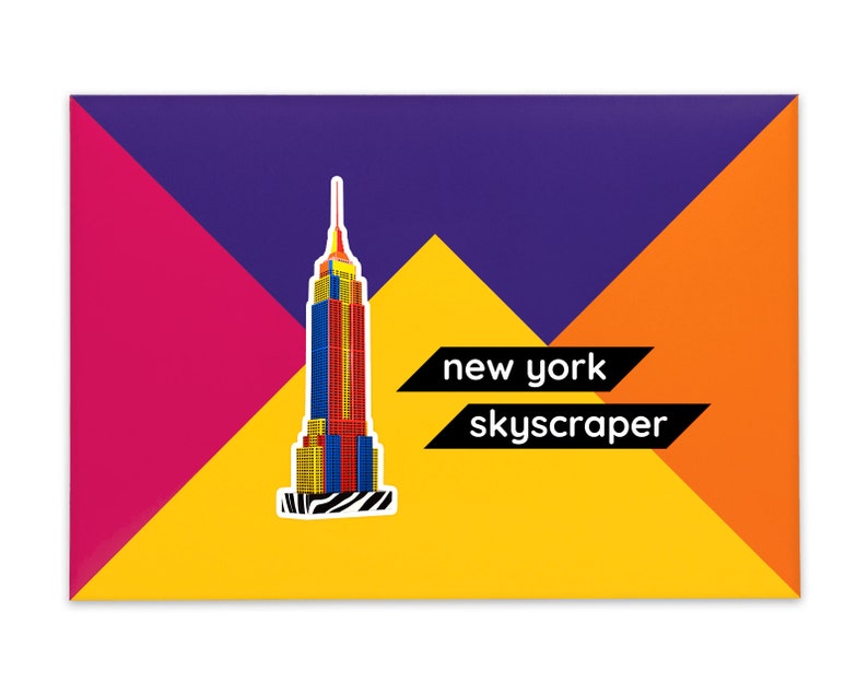Product packaging for the New York Skyscraper paper model kit. The bright coloured cardstock envelope features four large triangles in yellow, magenta, purple and orange with an image of a finished model at the centre and the product title below.