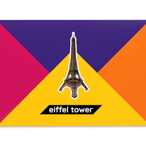 Product packaging for the Eiffel Tower paper model kit. A recangular bright coloured cardstock envelope features four large triangles in yellow, magenta, purple and orange with an image of a finished model at the centre and the product title below.