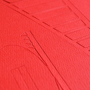 Closeup of a bright red die-cut cardstock sheet with parts to be easily removed for building Golden Gate bridge scale model out of PaperLandmarks paper model kit.
