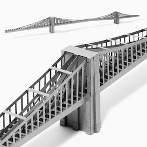 Könnte beinhalten: Ein graues Papiermodell einer Hängebrücke. Die Brücke besteht aus Pappe und hat ein detailliertes Design. Das Modell wird aus zwei Perspektiven gezeigt, einmal von oben und einmal von der Seite.