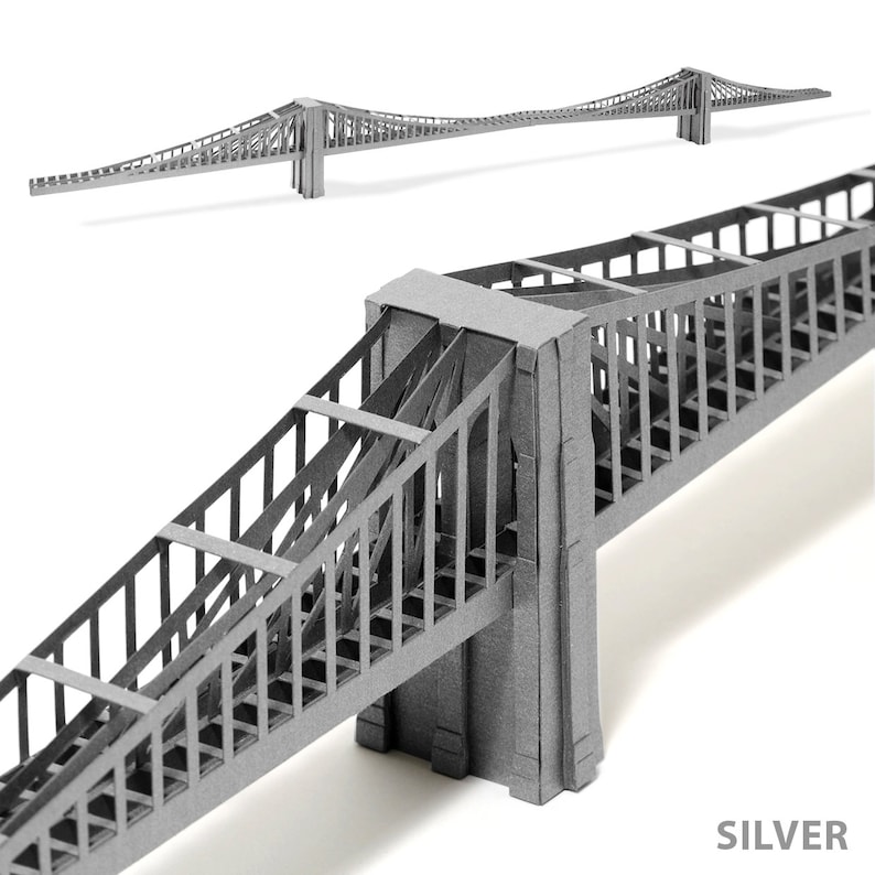 Combination of a closeup of a part and a diagonal view of entire 3d scale model of the Brooklyn Bridge, made out of silver perlescent die-cut cardstock parts. The model features two bridge towers, a deck and cables.