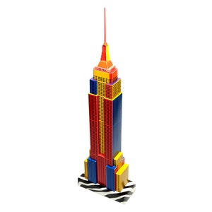 Assembled 3d paper model of the Empire State building of New York. The model features a black and white base, along with rows of vertical red, yellow, and blue strips layered along its facades.