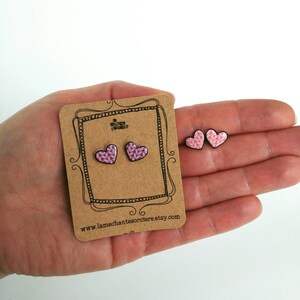 May include: A pair of pink knit heart-shaped earrings on a card with the text "www.lamechantesorciere.etsy.com".