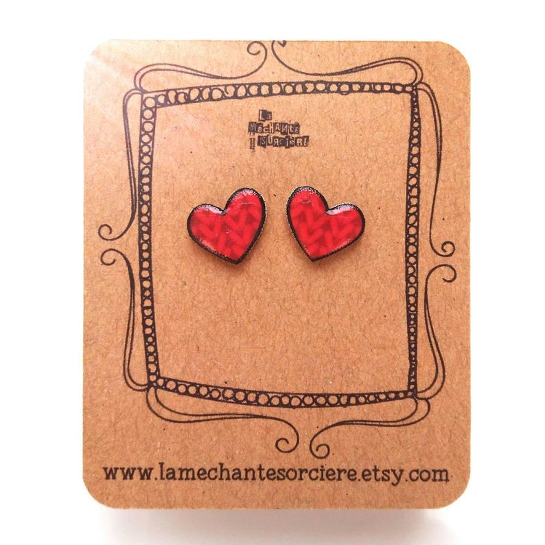 May include: A pair of red heart-shaped stud earrings with a textured pattern. The earrings are displayed on a brown card with a white border and the text "www.lamechantesorciere.etsy.com".