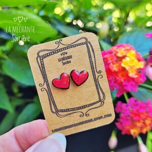May include: A pair of red heart-shaped earrings on a brown card with the text "La M&eacute;chante Sorci&egrave;re".