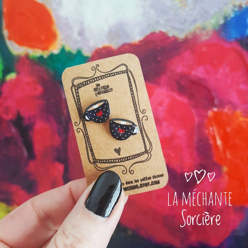 Pu&ograve; includere: Un paio di orecchini a forma di tazza da caff&egrave; nera e rossa con un motivo a cuore bianco. Gli orecchini sono su una carta con il testo "La M&eacute;chante Sorci&egrave;re" e "dans les petites choses".
