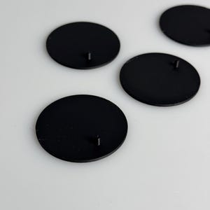May include: Four black round plastic bases with a small metal pin in the center of each.
