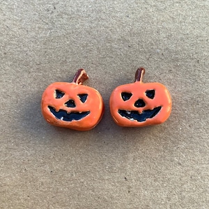 May include: Two small orange ceramic pumpkin figurines with black painted jack-o'-lantern faces.