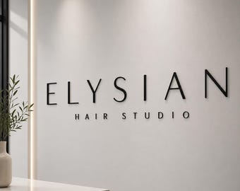 May include: A wall-mounted sign featuring the black, three-dimensional lettering ELYSIAN HAIR STUDIO. The text is displayed in a clean, sans-serif font against a smooth, light-colored wall, with a vertical light strip visible on the left side.