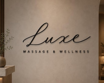 Puede incluir: Un letrero de pared que presenta el texto en cursiva negra Luxe sobre el texto en mayúsculas negras MASSAGE & WELLNESS. La señalización se muestra sobre una superficie de pared lisa y de color claro, creando un punto focal claro y legible.