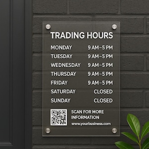 May include: A transparent acrylic sign showing business trading hours, fixed to a dark grey brick wall. The sign details opening times for each day, with a QR code and website address for further information.