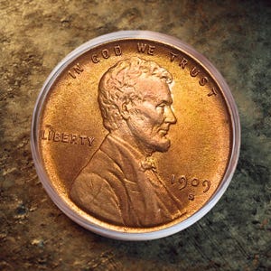 Puede incluir: Primer plano de un centavo Lincoln de 1909 de color cobre, protegido en un estuche de plástico transparente. La moneda presenta un perfil de Abraham Lincoln, con las inscripciones "IN GOD WE TRUST" y "LIBERTY". El año "1909" también es visible.