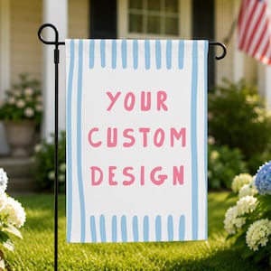 May include: A rectangular garden flag featuring a white center with the pink text "YOUR CUSTOM DESIGN" in a sans-serif font. The flag has vertical light blue stripes along the left and right edges and is mounted on a black metal stand.