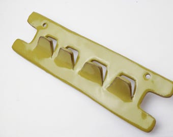 May include: A yellow ceramic wall-mounted rack with four hooks. The rack is designed to hold items like towels or keys.