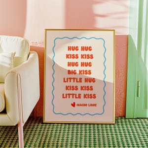 Może przedstawiać: Oprawiony wydruk artystyczny ze złotą obwódką. Wydruk zawiera słowa "HUG HUG, KISS KISS, HUG HUG, BIG KISS, LITTLE HUG, KISS KISS, LITTLE KISS" w czerwonym i niebieskim tekście na jasnoróżowym tle. Tekst "-NACHO LIBRE" znajduje się na dole.