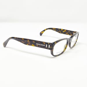 May include: A pair of Giorgio Armani eyeglasses with a tortoiseshell pattern. The frames are rectangular with clear lenses. The brand name is visible on the temple. The glasses are set against a white background.