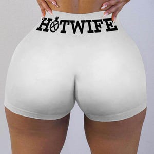 May include: White athletic shorts with the text "HOTWIFE" printed in black across the waistband. The shorts are form-fitting and made of a smooth fabric.