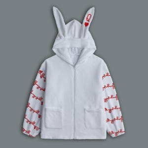 Puede incluir: Sudadera blanca con cremallera, orejas de conejo en la capucha y detalles de vid de rosas rojas en las mangas. La capucha presenta un corazón rojo y la letra "Q". Se ven dos bolsillos delanteros.