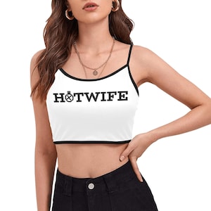 May include: White crop top with black trim and spaghetti straps. The top features the text "HOTWIFE" in bold black letters. The design includes a graphic of a ring with a diamond.
