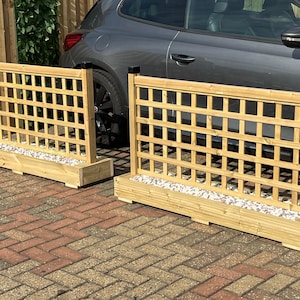 May include: Two rectangular wooden planter boxes with integrated square lattice trellis panels. Each planter features light brown natural wood construction, a rectangular base filled with small white and grey decorative stones, and black post caps.