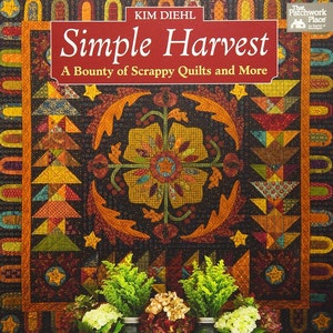 May include: A book titled "Simple Harvest: A Bounty of Scrappy Quilts and More" by Kim Diehl. The cover features a colorful quilt with a floral design and autumnal colors. The quilt is displayed against a dark background with fall foliage and pumpkins in the foreground.