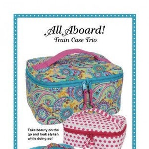 May include: Three train case sewing patterns with the text "All Aboard! Train Case Trio". The largest case is a paisley print with a turquoise zipper and pink handle. The medium case is pink with white polka dots and a white zipper. The smallest case is turquoise with a white zipper and a white handle. The text "Patterns by Annie" and "www.ByAnnie.com" are at the bottom of the image.