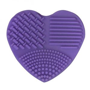 May include: Purple heart-shaped silicone makeup brush cleaning pad with three different textured surfaces for cleaning makeup brushes.