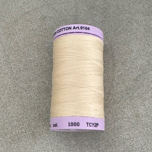 May include: A spool of beige cotton thread with a purple label that reads "High Cotton Art. 9104 col. 1000 TCY2P".