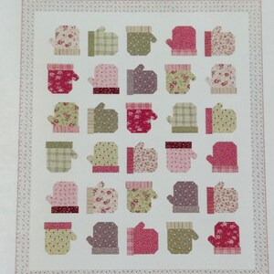 May include: A patchwork quilt featuring a repeating pattern of mittens in various colors and patterns. The mittens are primarily pink, green, and purple, with floral and plaid designs. The quilt has a white background and a patterned border.