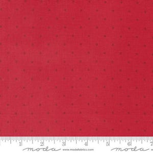 May include: Red fabric with small, evenly spaced brown dots. The fabric has a textured appearance and a ruler is visible along the bottom edge, marked with inches. The fabric is suitable for quilting and other craft projects.