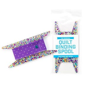 May include: A purple and white polka dot fabric spool with a colorful confetti design. The spool is labeled "The Original Quilt Binding Spool".