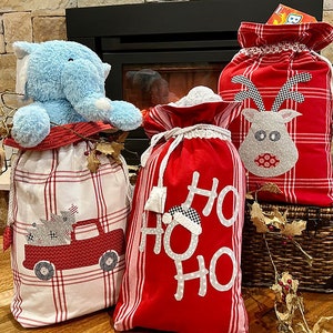 May include: Three Christmas stockings with different designs. One is red with a plaid pattern and a reindeer applique. Another is red with a white "Ho Ho Ho" design. The last one is white with a red plaid pattern and a red truck applique.