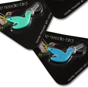 May include: Two turquoise and blue plastic needle threaders shaped like hummingbirds. Each threader is packaged on a black card with the text "le needle bird" and "needle threader with cutter".