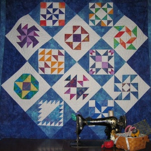 May include: A blue and white quilt with a variety of patchwork designs, including stars, pinwheels, and triangles. A sewing machine is in the foreground.