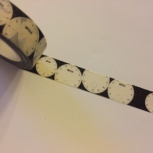 May include: A roll of black and white washi tape with a repeating pattern of clock faces. The clock faces are white with black numbers and the word "Swatch" printed on them.