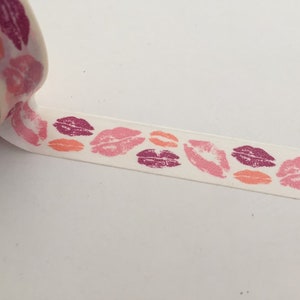 May include: A roll of white washi tape with a repeating pattern of pink, red, and orange lips.