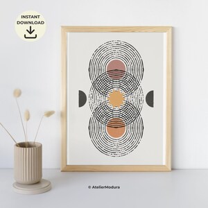 Op de afbeelding: Een ingelijste kunstdruk met een verticale opstelling van zwarte concentrische cirkels, een centrale gele zonvorm en twee donkergrijze halve cirkels aan de zijkanten. De achtergrond is gebroken wit en de print bevat de tekst AtelierModura.