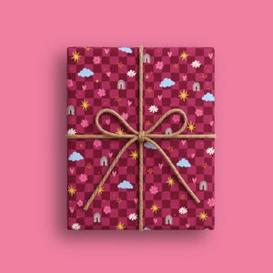 Könnte beinhalten: Ein rechteckiges Geschenk, eingewickelt in dunkelrosa und kastanienbraun kariertes Papier mit einem Muster aus hellblauen Wolken, gelben Sternen, rosa Blumen, kleinen Herzen und grauen Regenbögen, gebunden mit einer naturfarbenen Juteschnur.