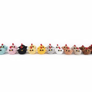 Könnte beinhalten: Eine Sammlung kleiner, gehäkelter Hühnerfiguren in verschiedenen Farben, darunter Grün, Blau, Rosa, Schwarz, Gelb, Grau, Weiß, Beige, Braun und Dunkelbraun. Jedes Huhn hat einen roten Kamm und kleine, dunkle Augen.