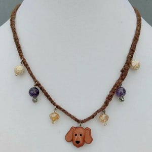 Colgante de botón de perro Cocker Spaniel hecho a mano con cuentas blancas y moradas trenzadas en un collar de cordón de cáñamo marrón oscuro.